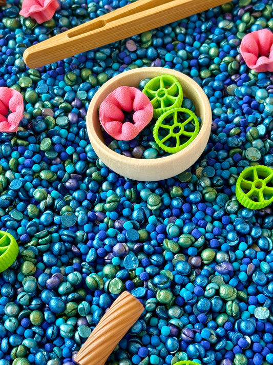 Wooden bowl and tweezers with pink flower and green wheel pasta on blue pond filler