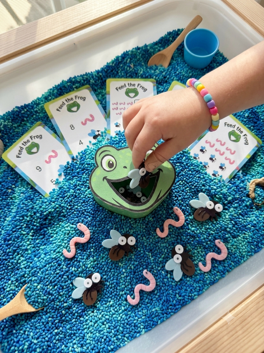 Child playing Feed the Frog counting game over a blue rice sensory bin