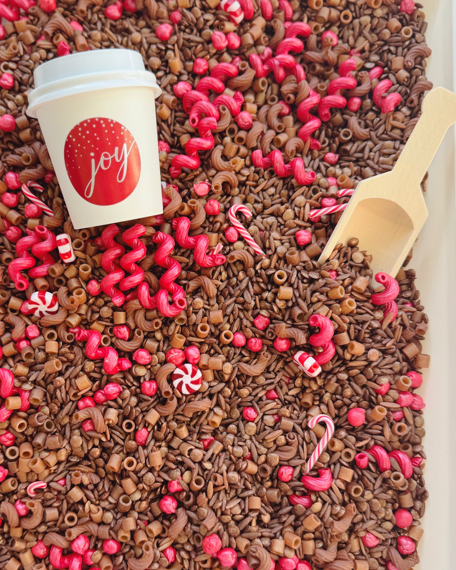 Hot Cocoa sensory bin with joy cup, wooden scoop, candy canes and pink and brown filler