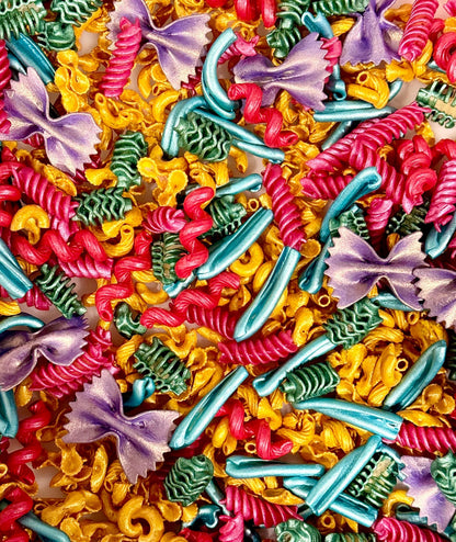 A colorful assortment of pasta shapes to be used as sensory bin filler. Pasta shapes include fusilli, farfalle, and elbow macaroni. The pasta is dyed in vibrant hues of red, yellow, teal, green, and purple. The image is a close-up, showcasing the variety of shapes and colors.
